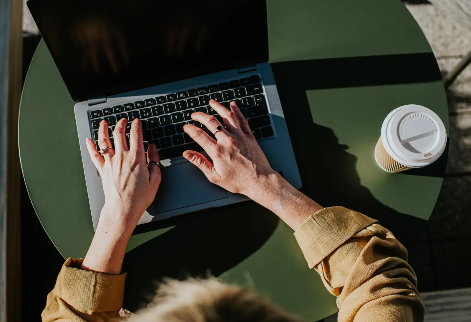 Hands typing on a laptop on a green café table beside a coffee cup